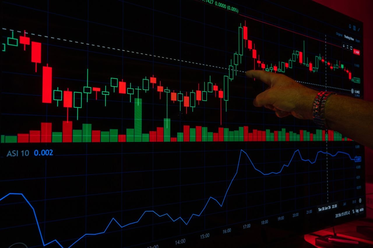 A hand points at a stock market graph on a digital screen, highlighting financial trading trends.